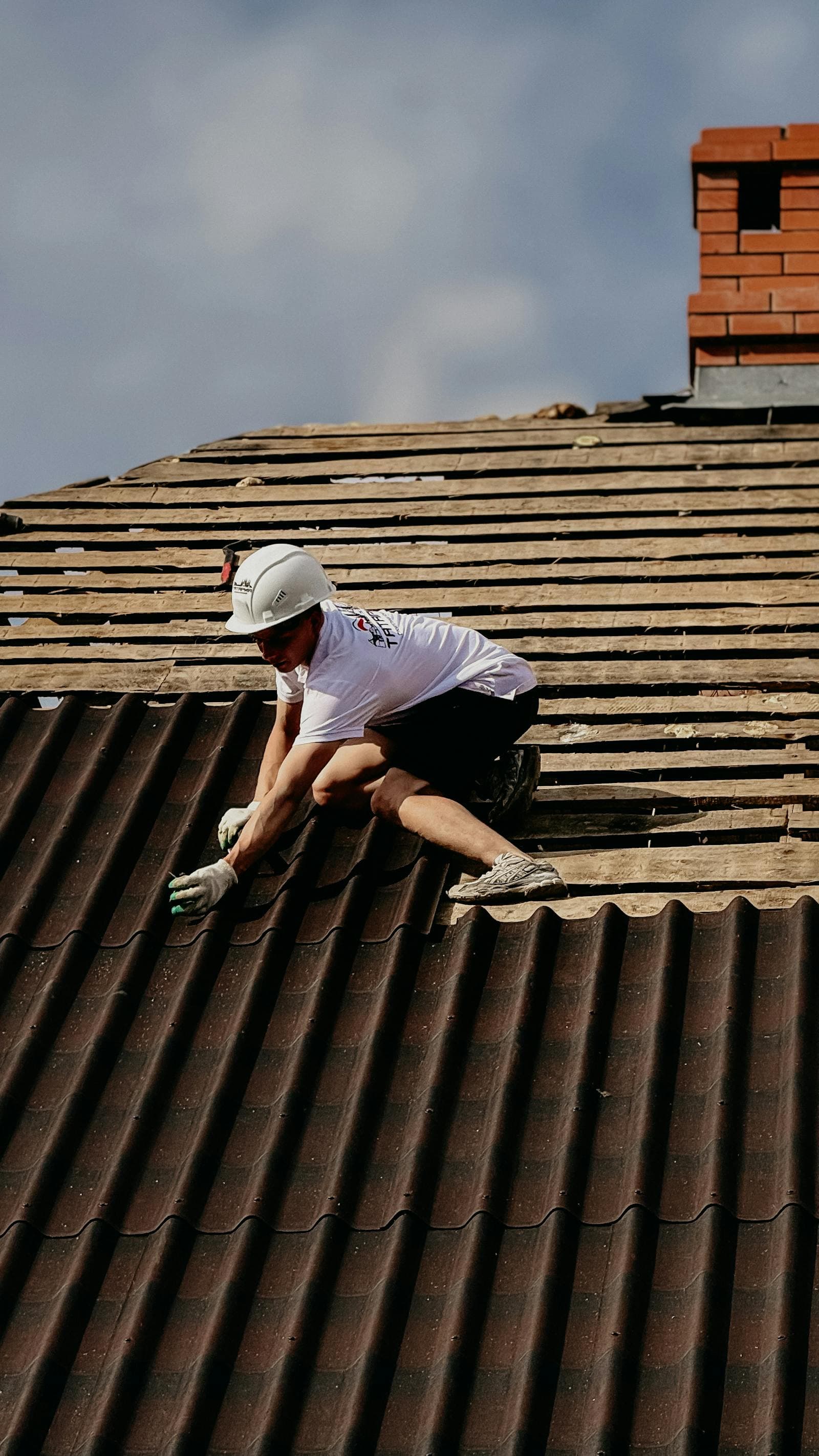 Roofer in a white hard hat working on a steep tile roof next to a chimney