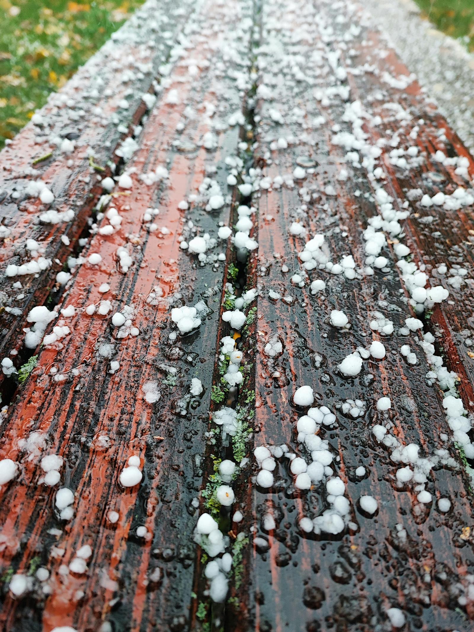 Hailstones scattered across a red wooden bench after a storm