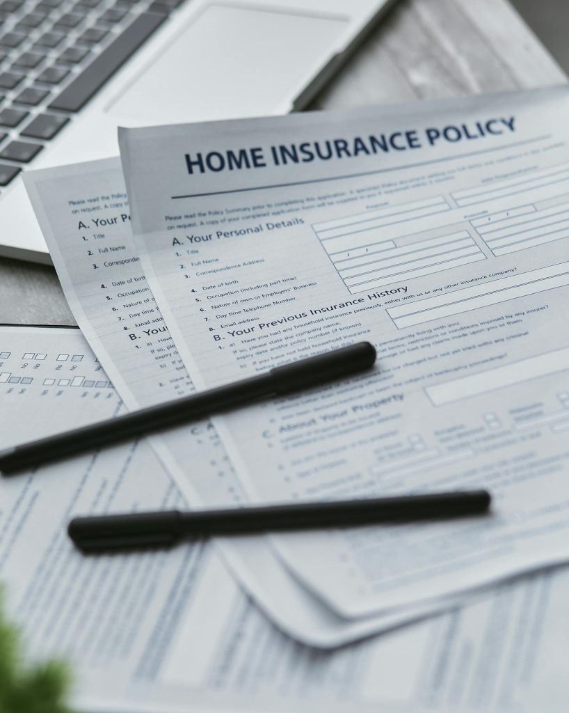 Home insurance policy paperwork on a desk with pens and a laptop