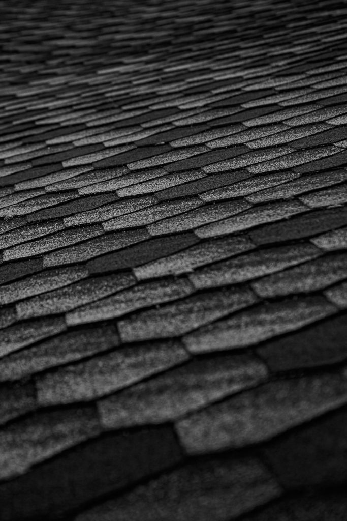 Close-up of dark asphalt shingles on a steep residential roof under Texas sun